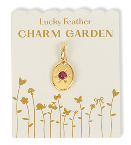 A gold pendant with a pink jewel on a card labeled 'Lucky Feather CHARM GARDEN' with flower and butterfly illustrations.