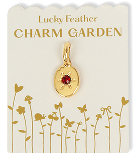 Gold pendant with red stone on a Lucky Feather Charm Garden display card.