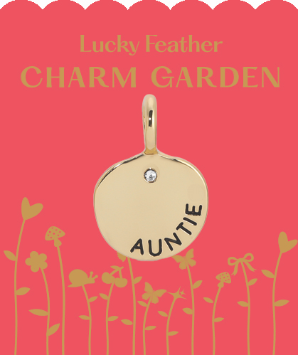 Close-up of a Lucky Feather Charm Garden 'Auntie' charm on a pink card with gold floral designs.