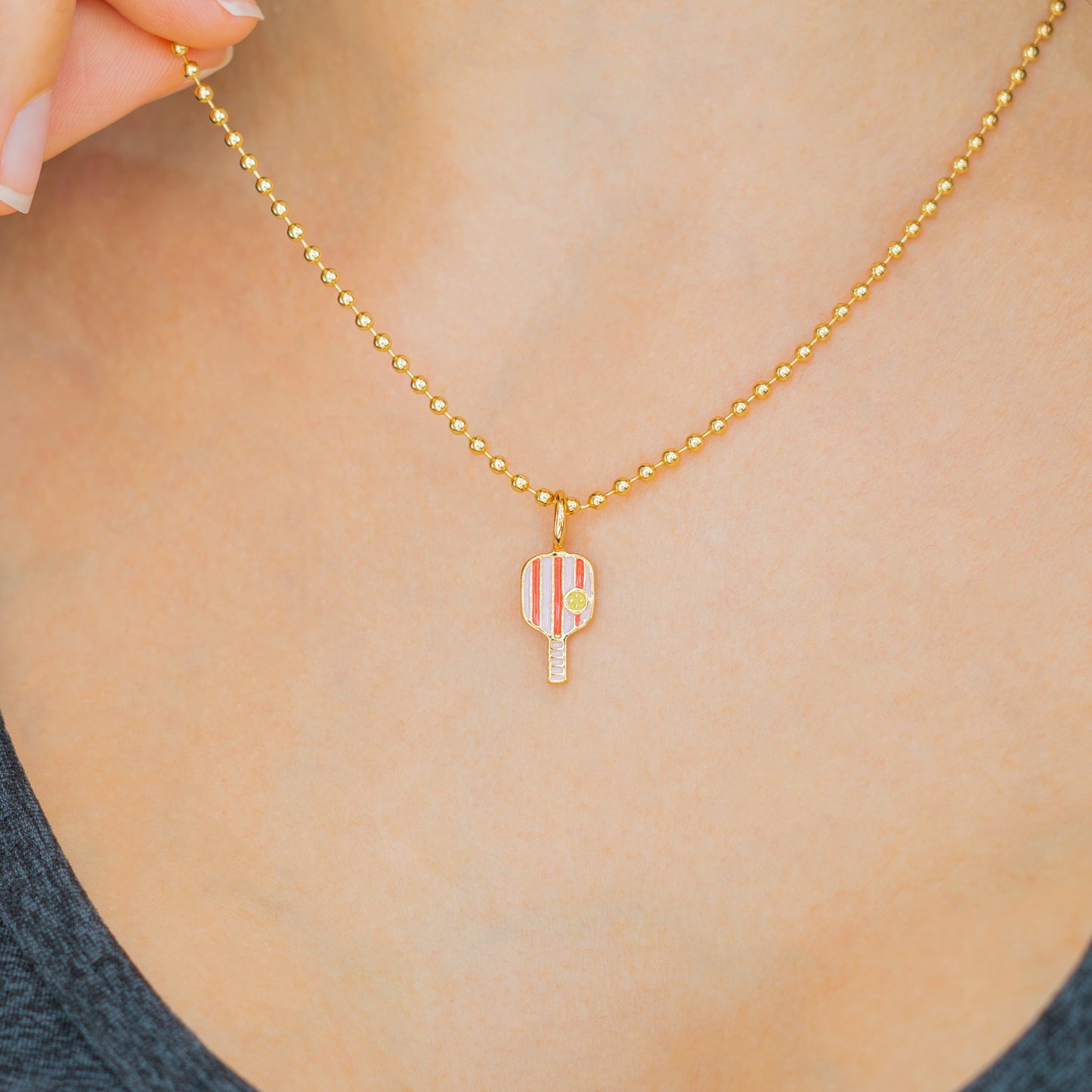 A woman wears a gold ball chain necklace with a pickleball paddle pendant.