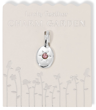 A silver 'Lucky Feather Charm Garden' pendant with a pink stone on a white card with an embossed floral design.