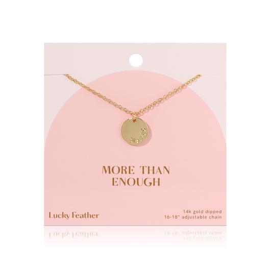 A 14k gold dipped necklace with a round pendant hangs against a pink card with 'MORE THAN ENOUGH' printed on it.
