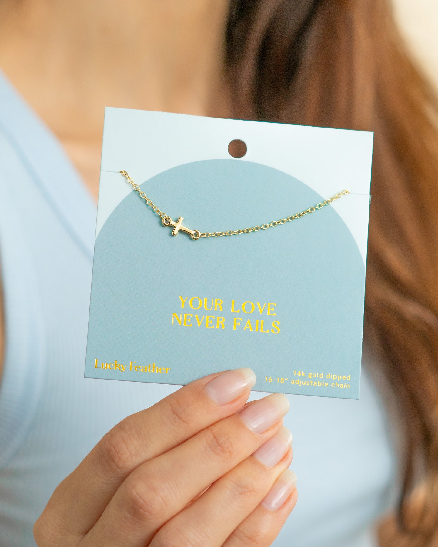 A woman holds a card with a gold cross necklace on it.
