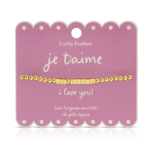 Gold beaded 'je t'aime' bracelet displayed on a pink scalloped card.
