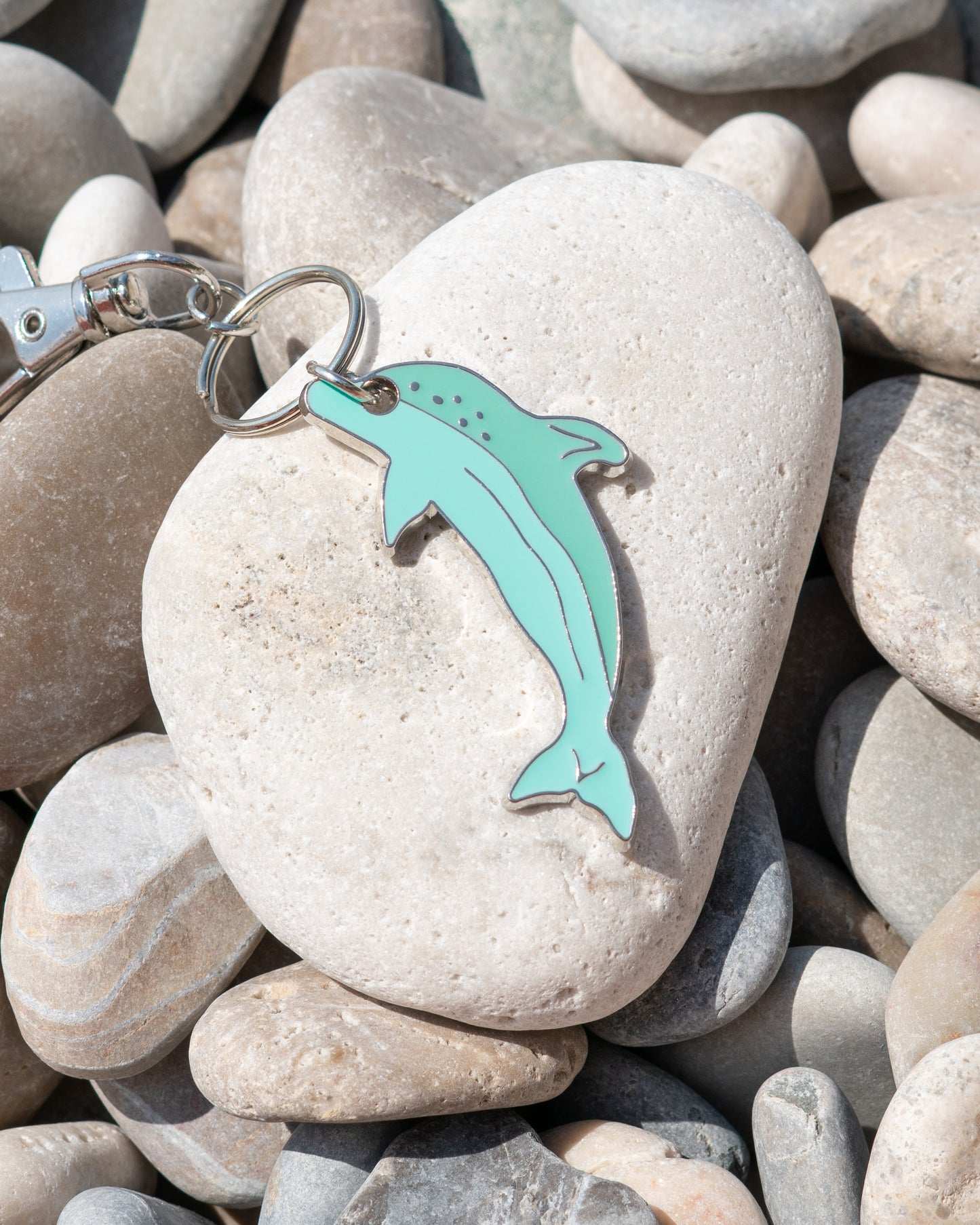 A light blue dolphin keychain rests on light-colored rocks.