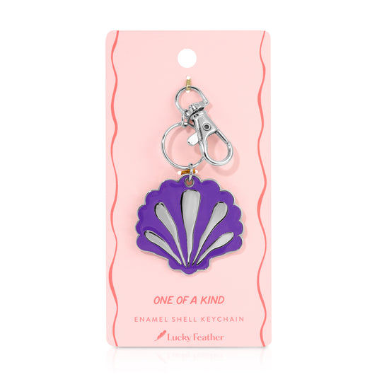 A purple enamel shell keychain with a silver clasp on a pink display card.