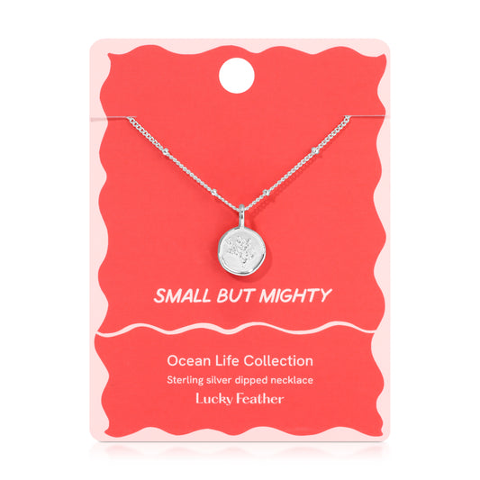 A silver necklace with a round pendant featuring a feather design, displayed on a red and pink card that reads 'SMALL BUT MIGHTY' and 'Lucky Feather'.