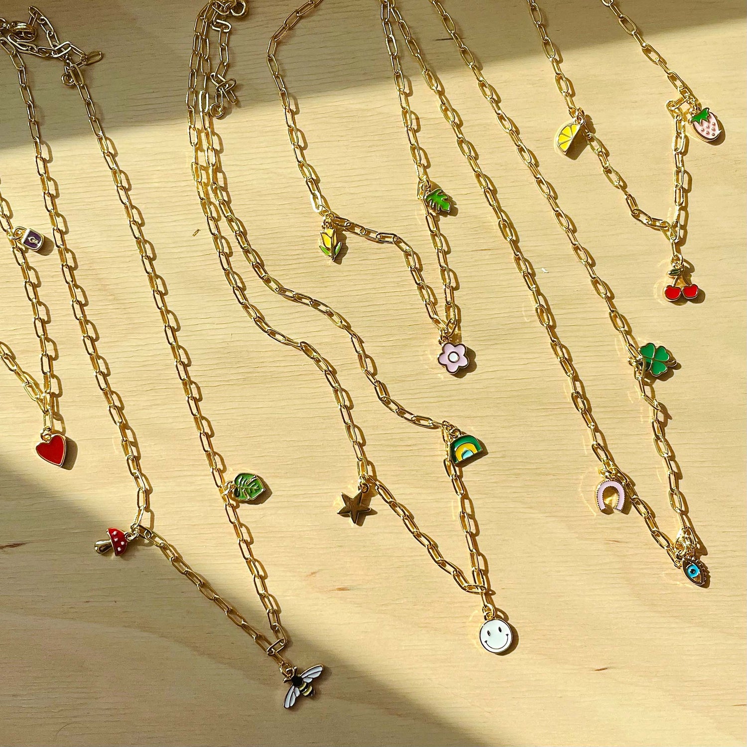 Several gold charm necklaces are arranged on a wooden surface, with sunlight casting shadows.