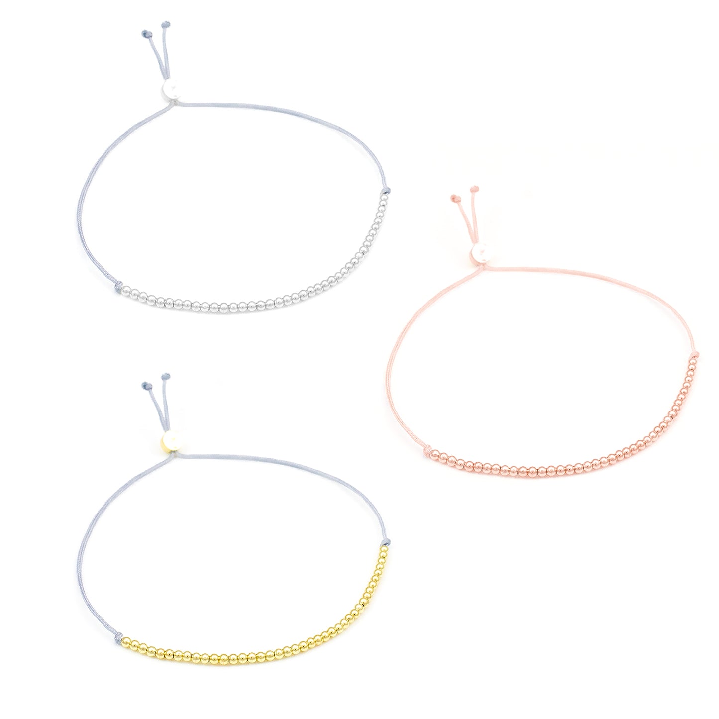 Three cord bracelets, silver, pink, and gold, are displayed on a white background.