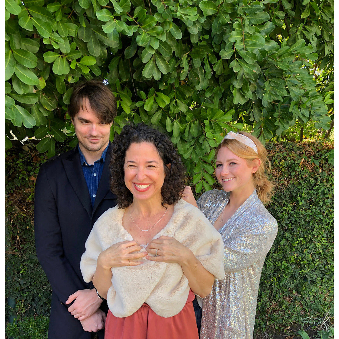 Three people pose for a photo in front of greenery.
