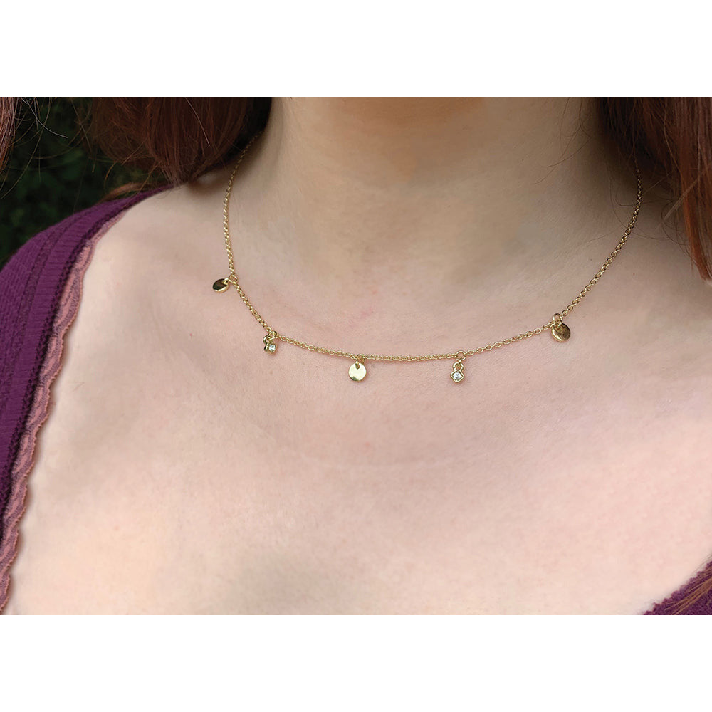 A person wears a gold chain necklace with small, dangling charms.