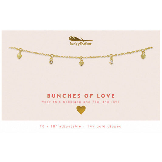 A gold-toned necklace with heart and stone charms on a pink card.
