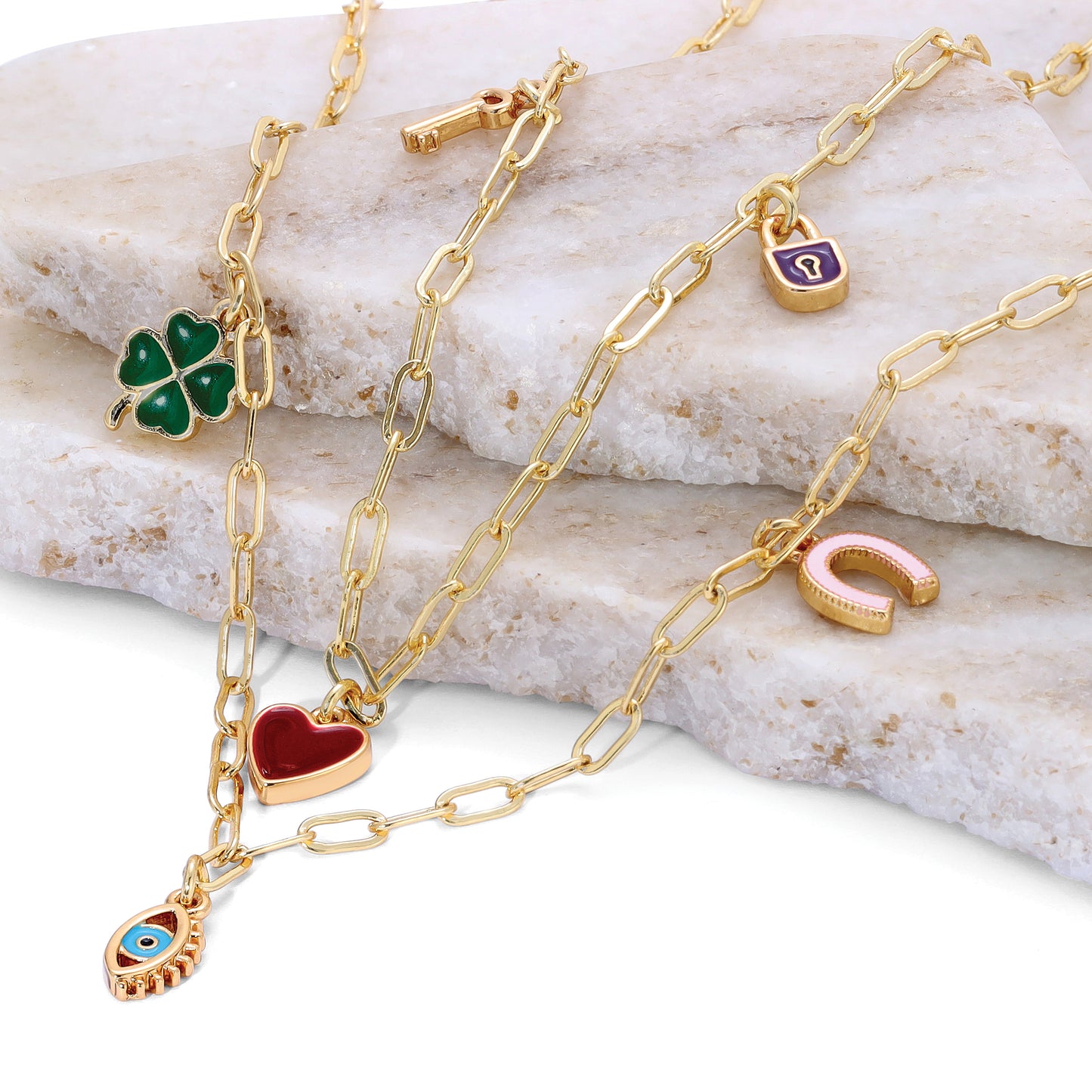 A gold chain necklace with multiple lucky charms is displayed on a white stone surface.