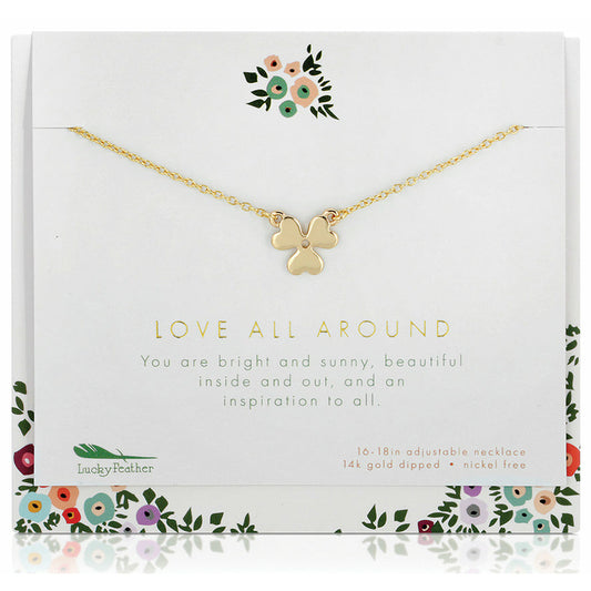A gold-colored clover necklace on a card with floral designs and inspirational text.