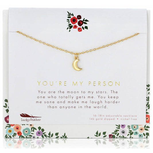 A gold-colored crescent moon pendant hangs from a thin chain displayed on a card with floral accents and the text 'You're my person.'