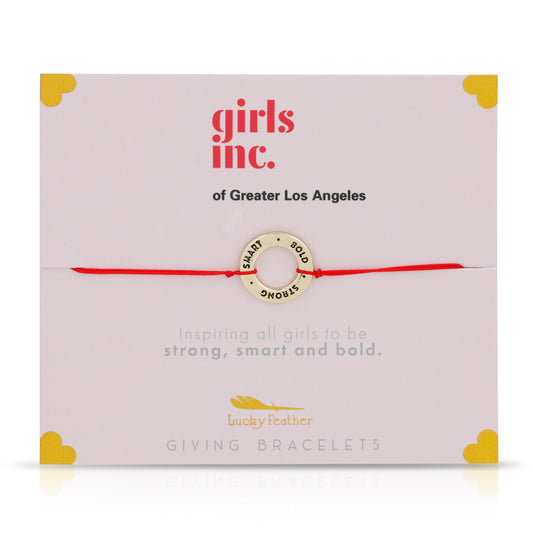 Girls Inc. giving bracelet with a gold charm on a red string displayed on a card.