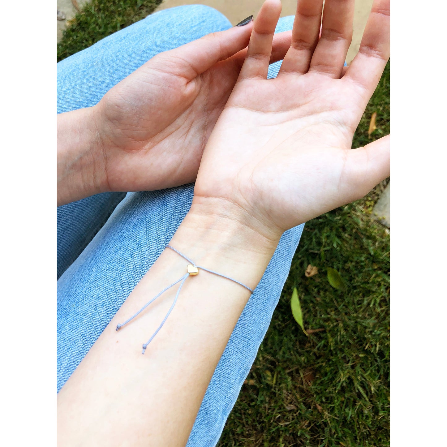 Close-up of a person's hands wearing a string bracelet with a small golden heart on their wrist.