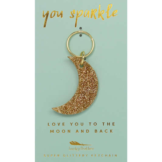 A crescent moon keychain with gold glitter is displayed on a light green card with gold lettering.