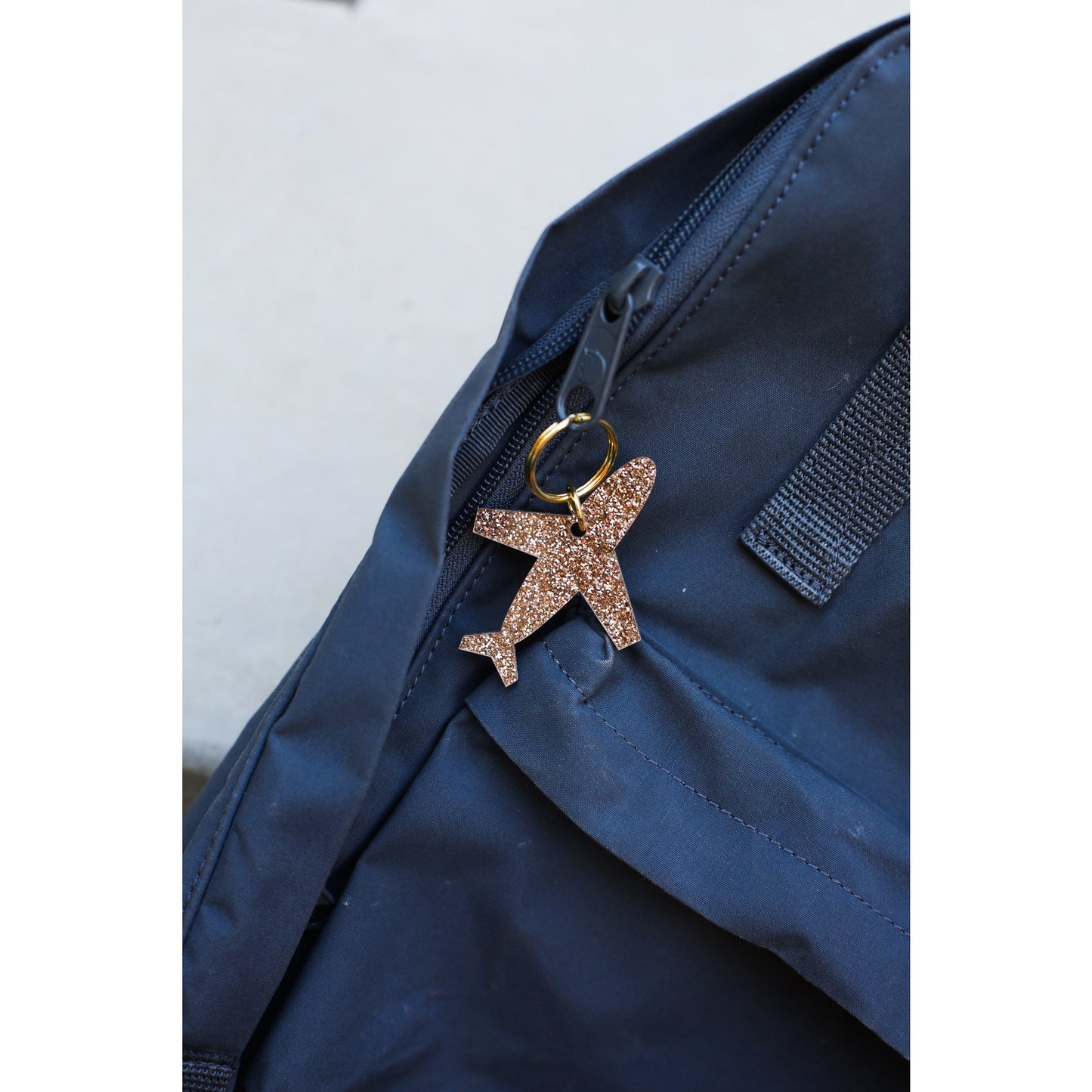 A bronze glitter airplane keychain hangs from the zipper of a dark blue bag.