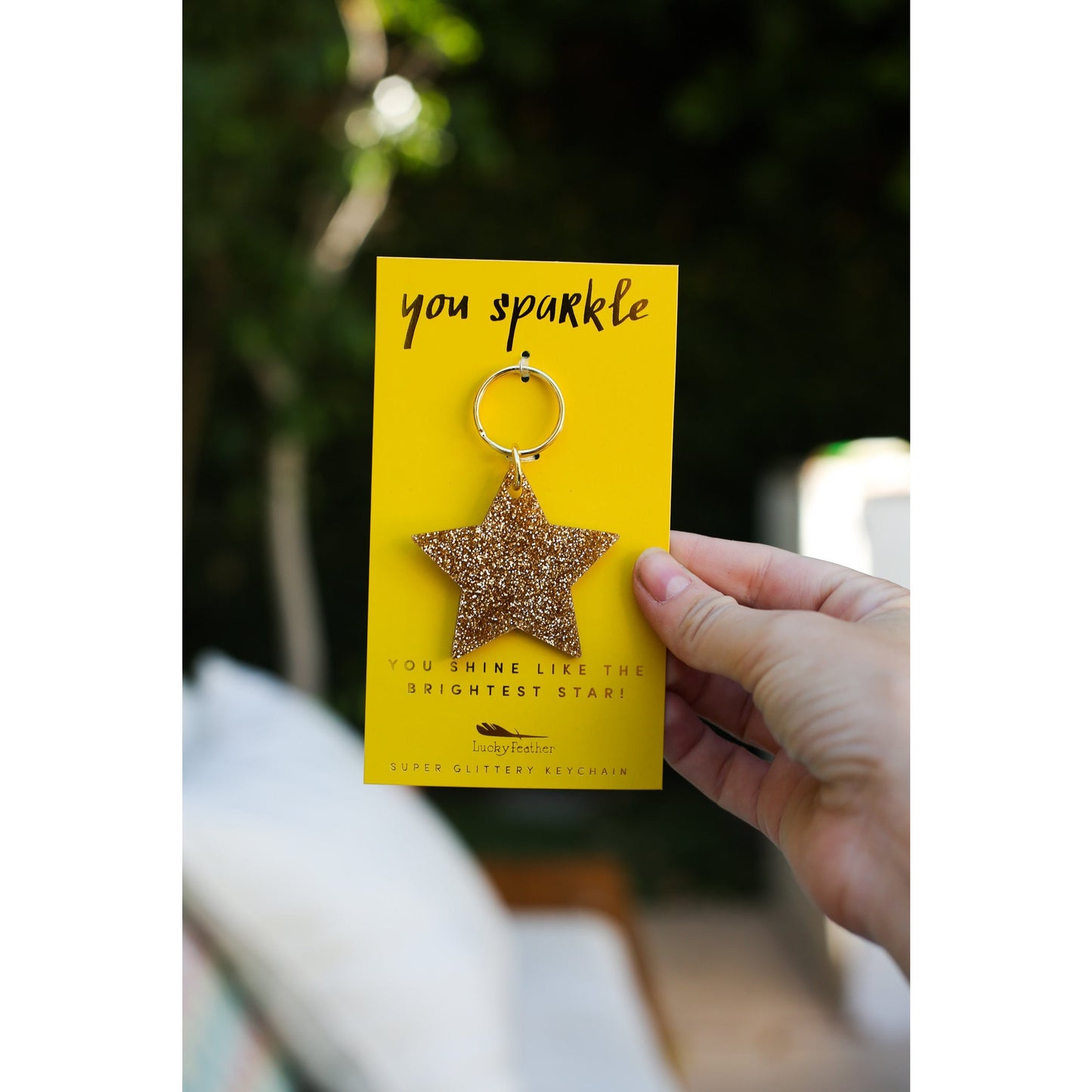 A hand holds a yellow card with a gold glittery star keychain attached.