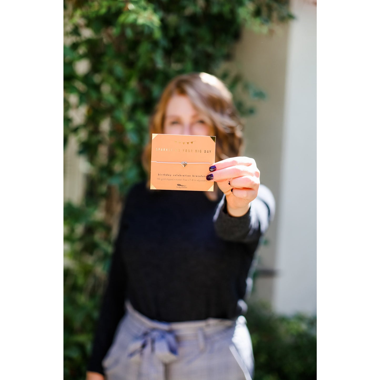 A person holds up a 'Sparkle On Your Big Day' birthday bracelet with a diamond charm.