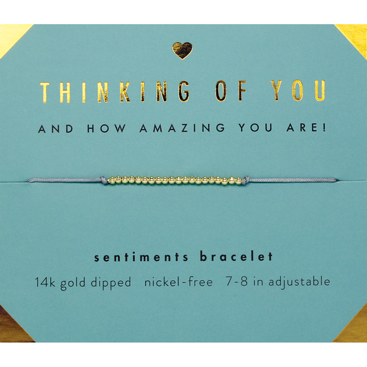 A 'Thinking Of You' sentiment bracelet with gold beads on a teal card.