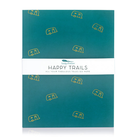 A teal notebook with yellow camper icons is secured with a white band labeled 'Lucky Feather HAPPY TRAILS ALL YOUR FABULOUS TALES GO HERE.'