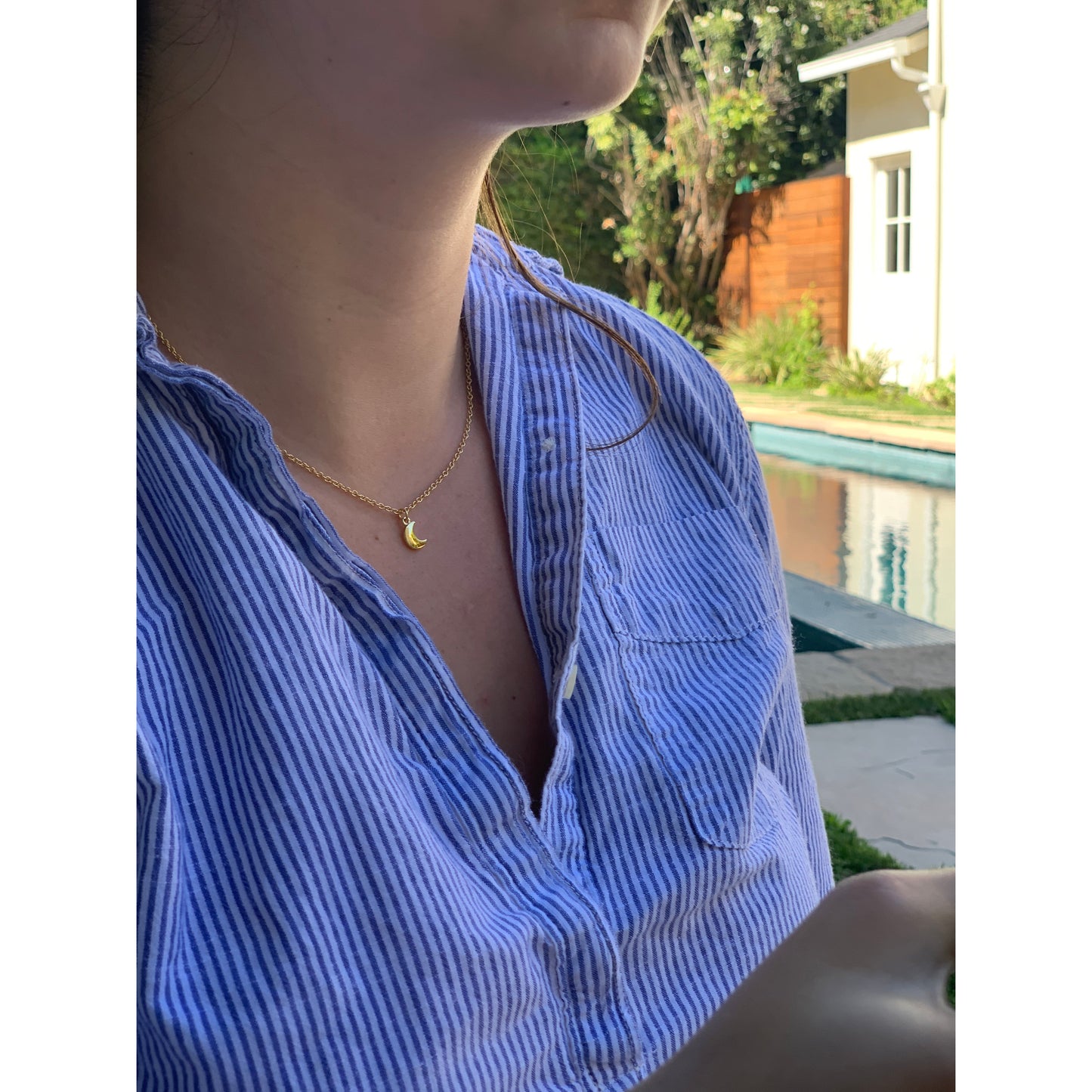 A person in a blue-and-white striped shirt wears a gold necklace with a crescent moon pendant.