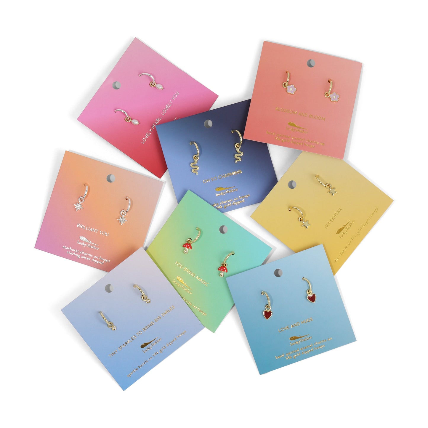 Several pairs of small hoop earrings with charms on colorful display cards are arranged on a white surface.