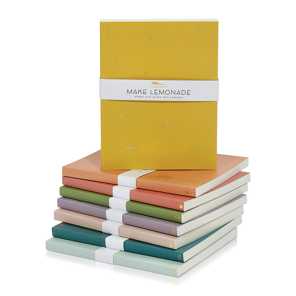A stack of colorful journals with a yellow notebook and a 'Make Lemonade' band on top.