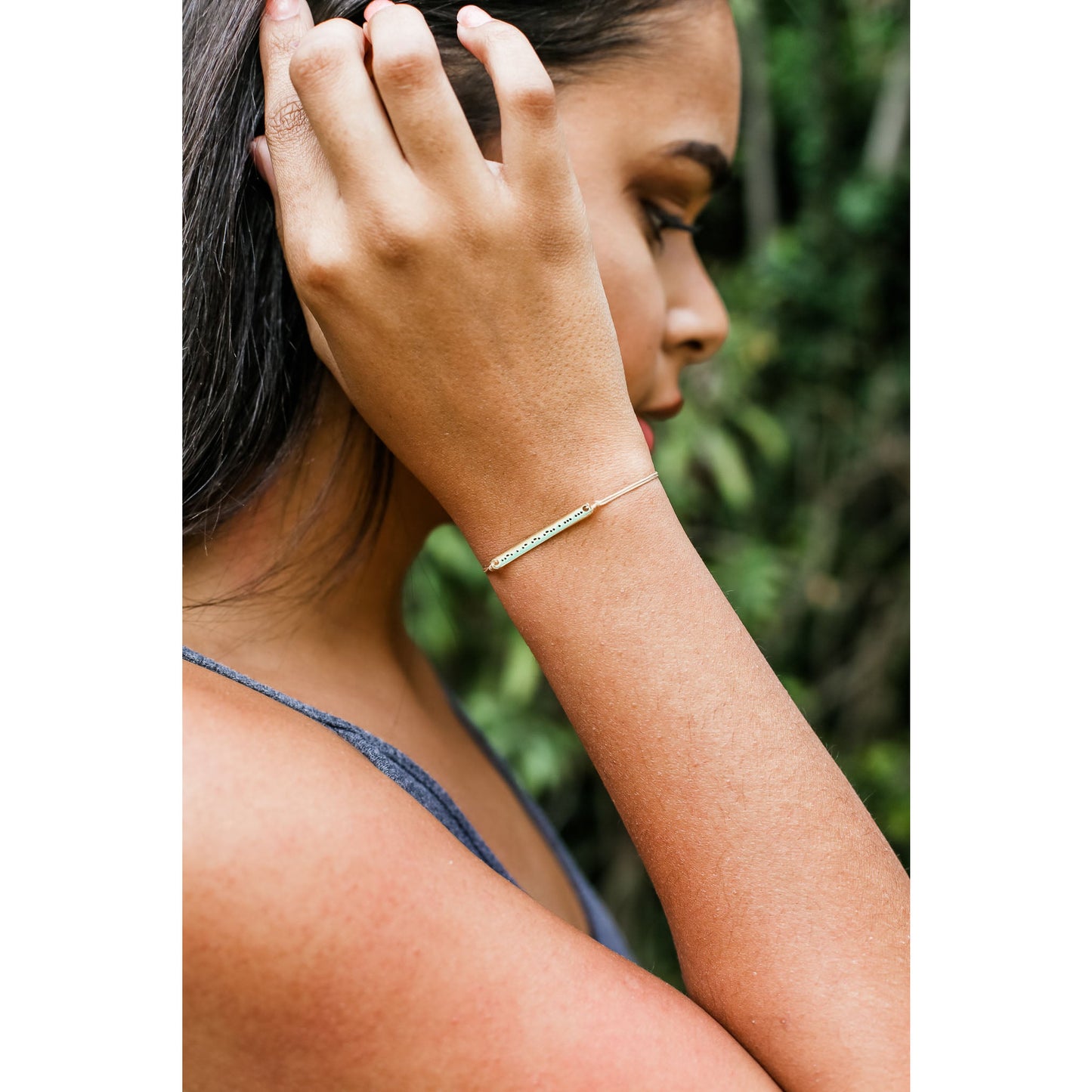 A person with dark hair and a blue tank top wearing a bracelet.