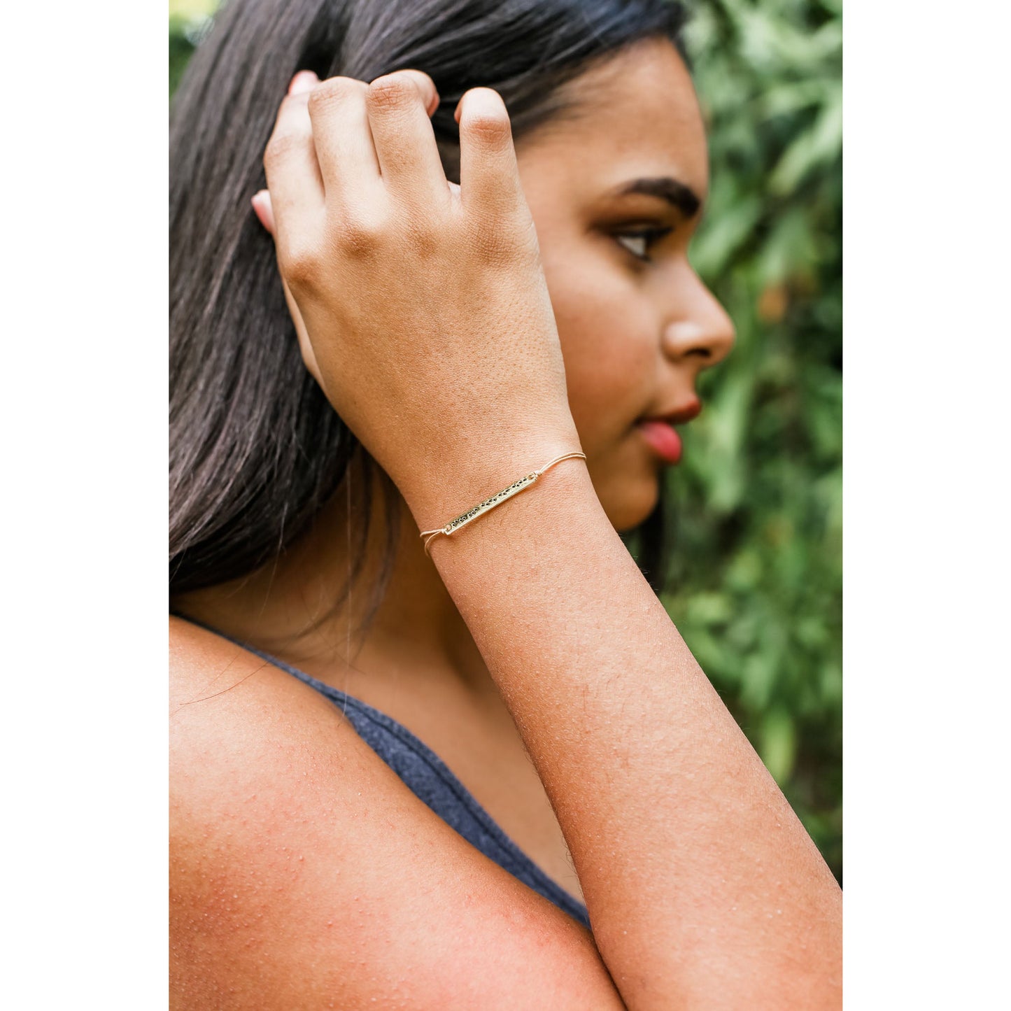 A person with long hair and a gold bracelet touches their hair while facing right.
