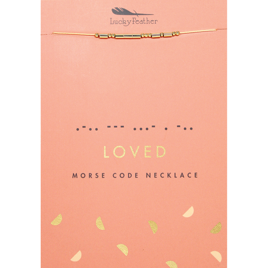 A 'Lucky Feather' necklace with beads representing morse code spelling out 'loved' displayed on the product's peach-colored packaging.