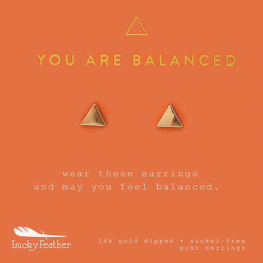 Two gold, triangular Lucky Feather post earrings on an orange card that reads 'YOU ARE BALANCED.'