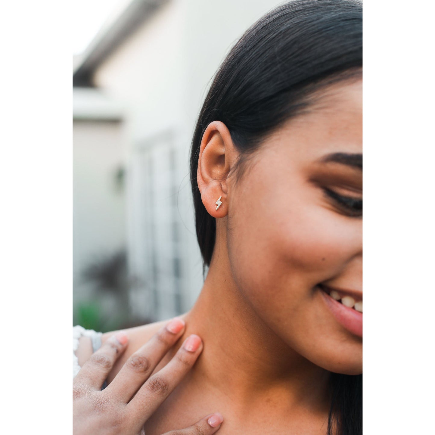 A woman smiles while wearing a lightning bolt stud earring.