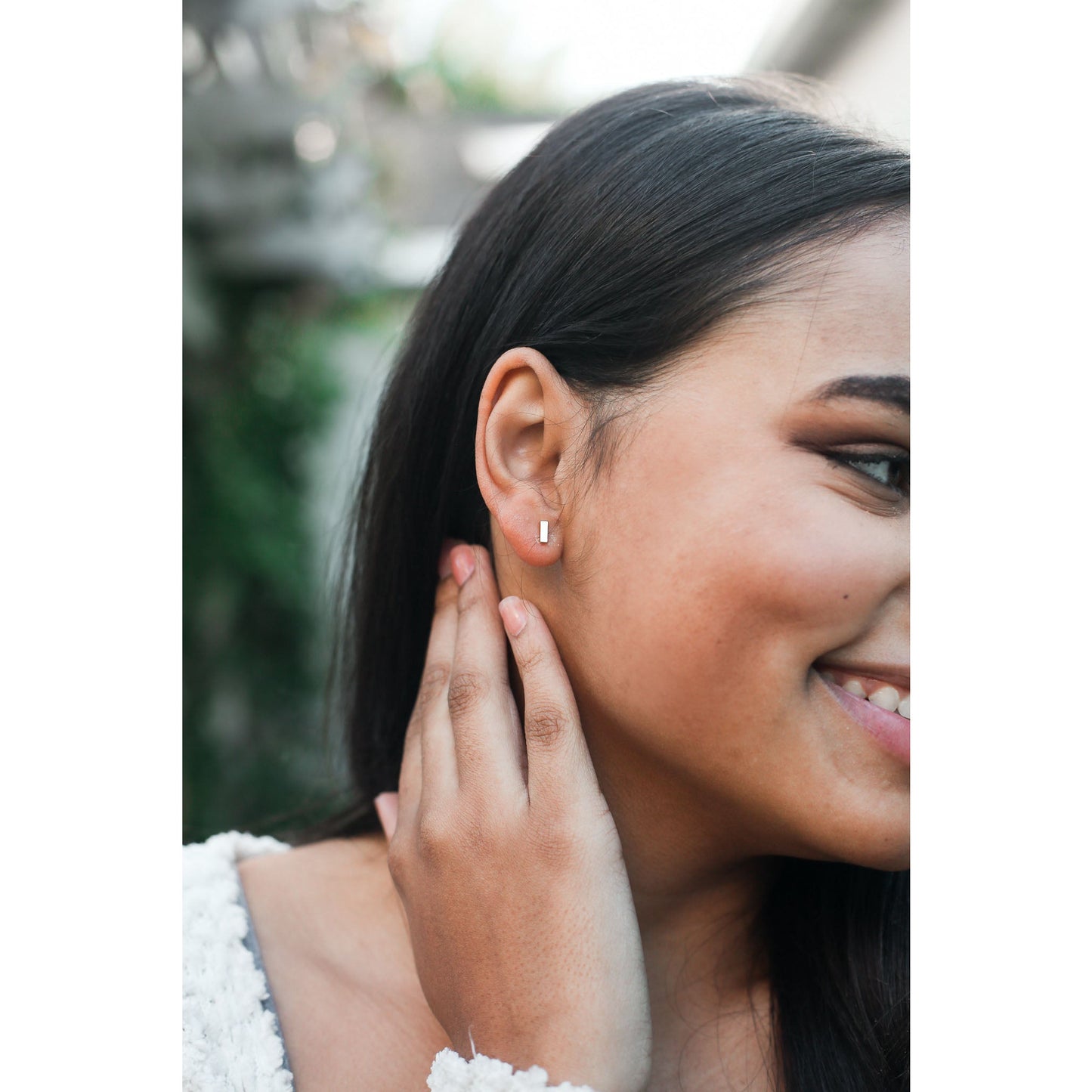 Close-up of a smiling woman with a silver bar earring.