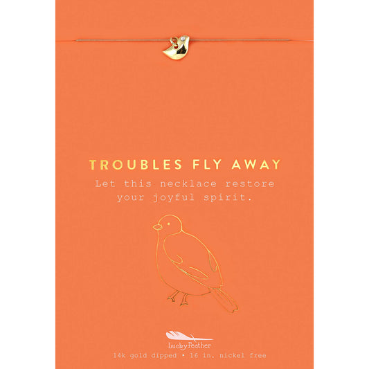 An orange card with a gold-colored bird charm, a gold-colored bird outline, and the words 'Troubles Fly Away.'