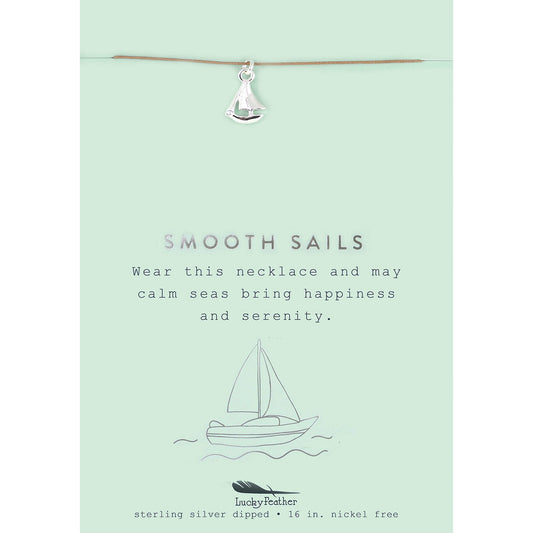 A silver sailboat charm necklace hangs on a card with a sailboat illustration and the phrase 'Smooth Sails.'