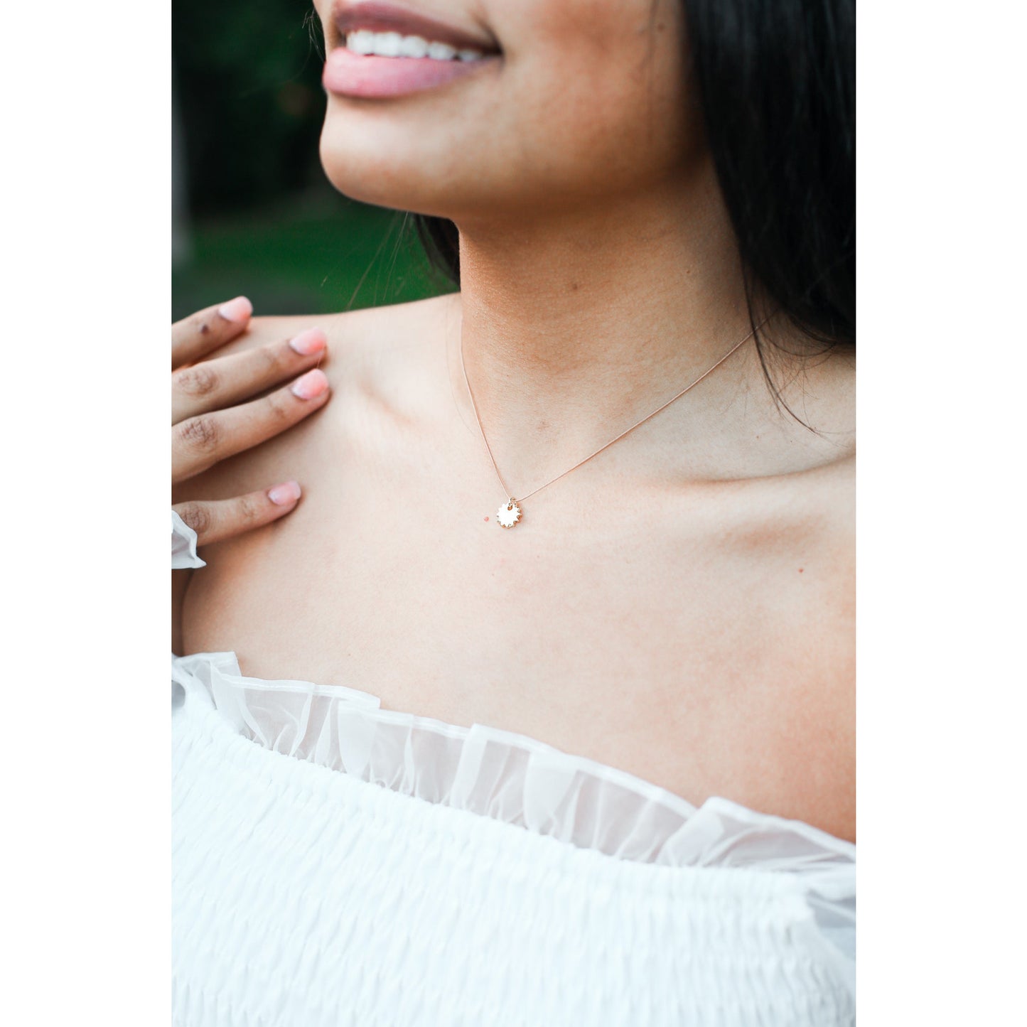 A woman with black hair wearing a gold sun pendant necklace.