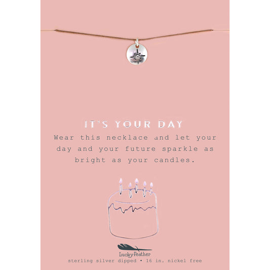 A necklace with a round pendant on a pink card that says 'It's Your Day'.