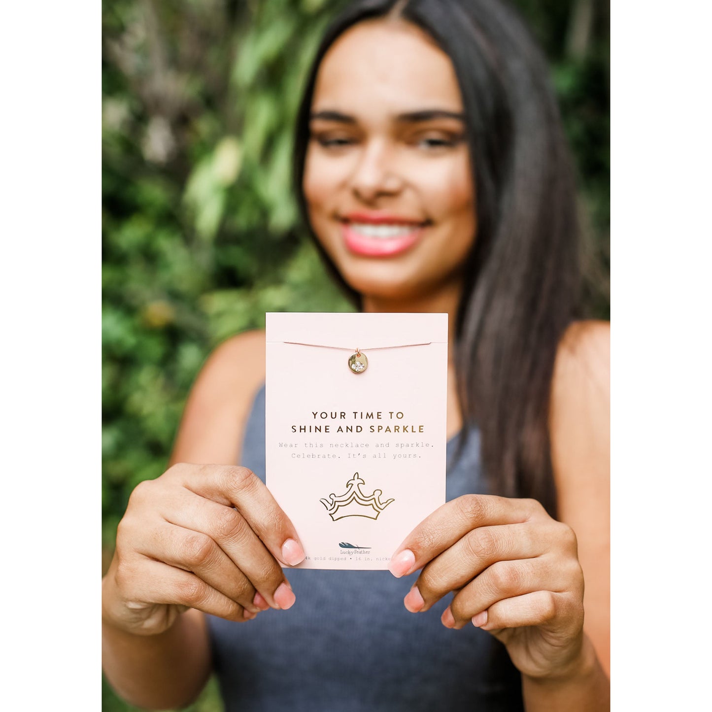A smiling woman holds up a jewelry card with a necklace attached.