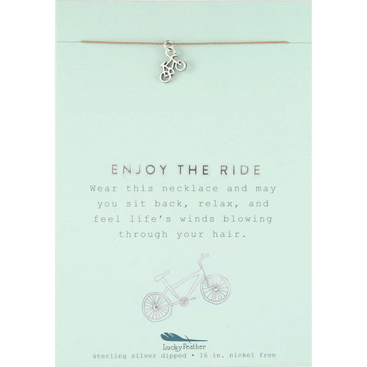 A 'Lucky Feather' necklace with a bicycle charm on a card that reads 'Enjoy the Ride.'