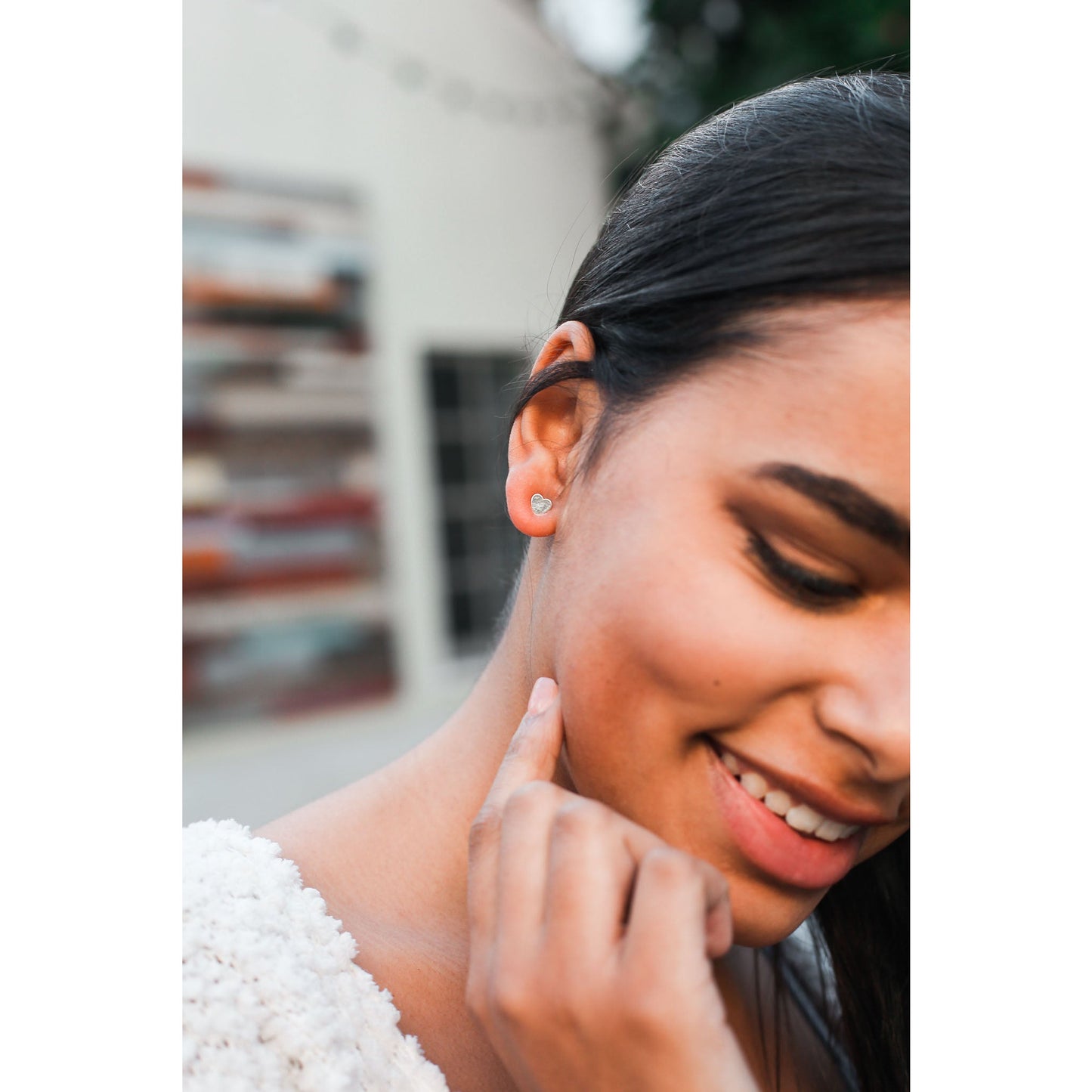 Close-up of a smiling woman with a heart-shaped earring touching her neck.