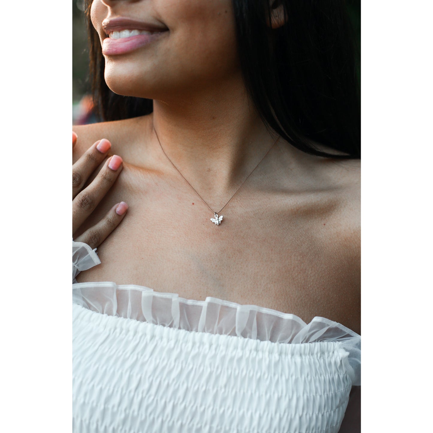 A woman in a white off-the-shoulder top wears a bee pendant necklace.