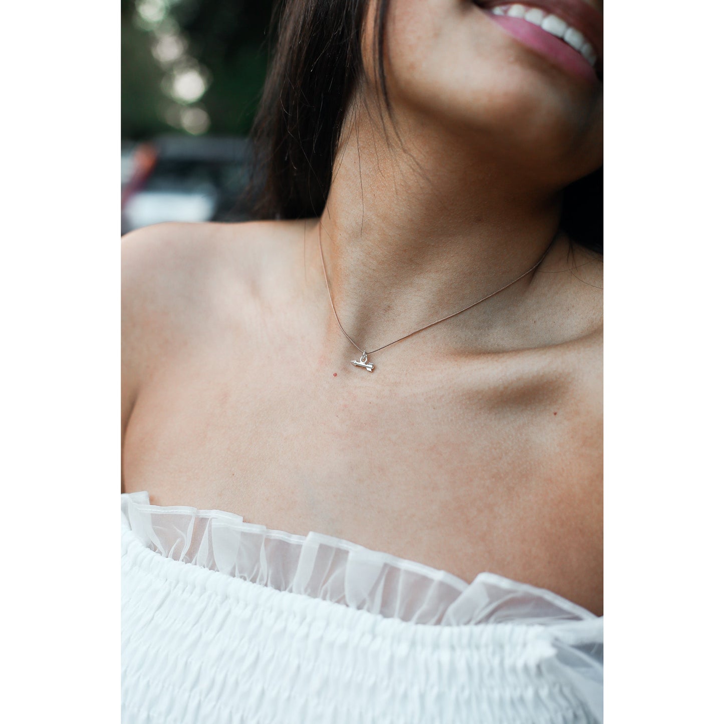 A person wearing a white, ruffled top and a delicate necklace with an arrow charm.