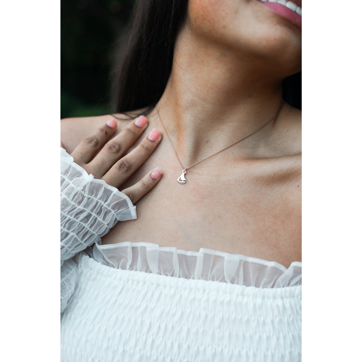 Person wearing a white ruffled top and a silver pendant necklace.