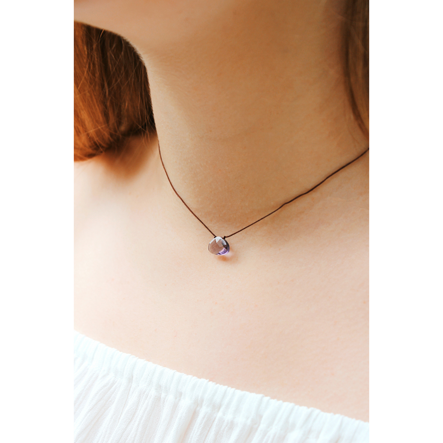 Person wearing a brown cord necklace with a teardrop shaped, purple pendant.